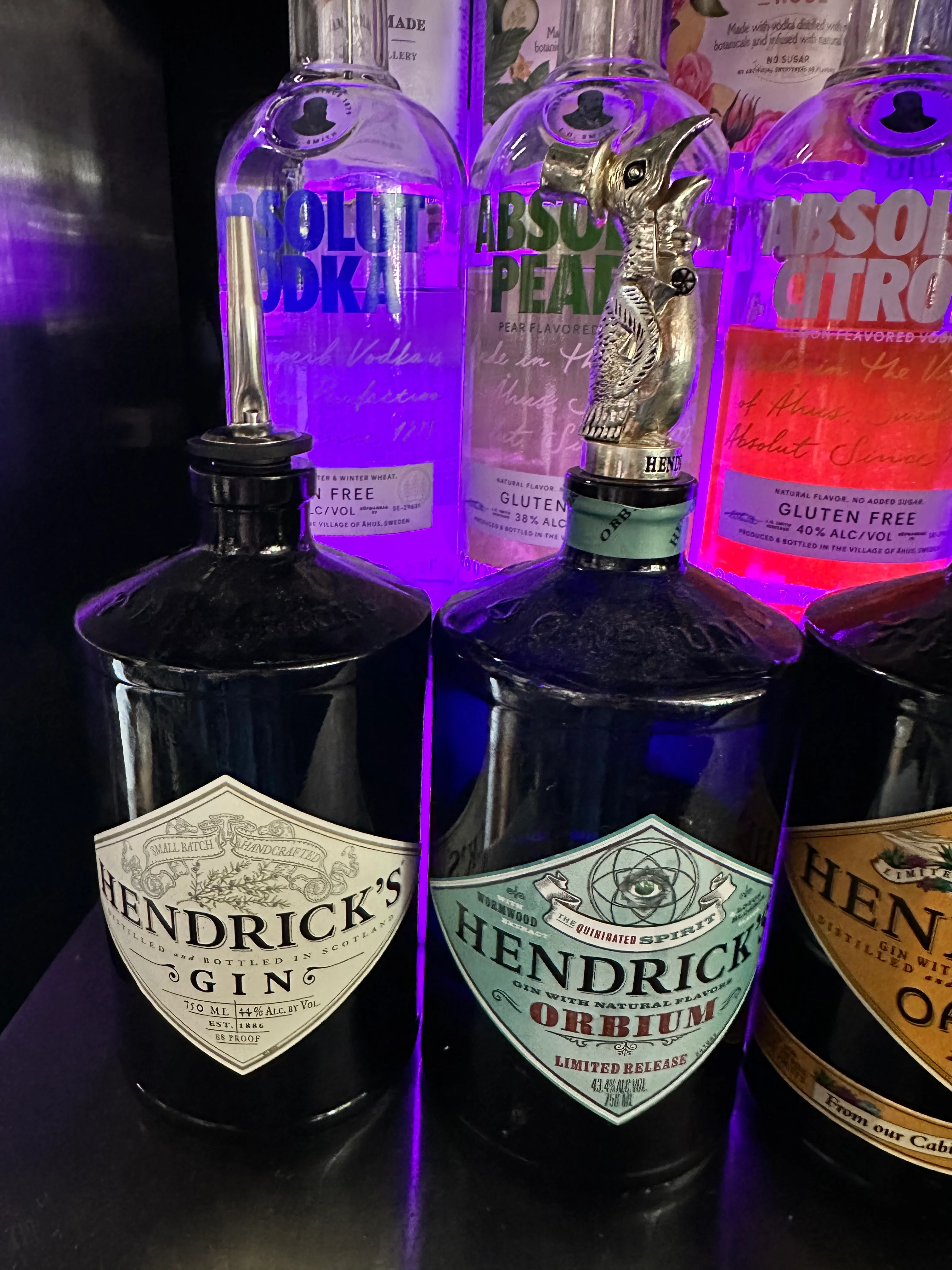A collection of unique liquor bottles featuring Hendrick's gin and flavored vodkas, illuminated with a purple light.