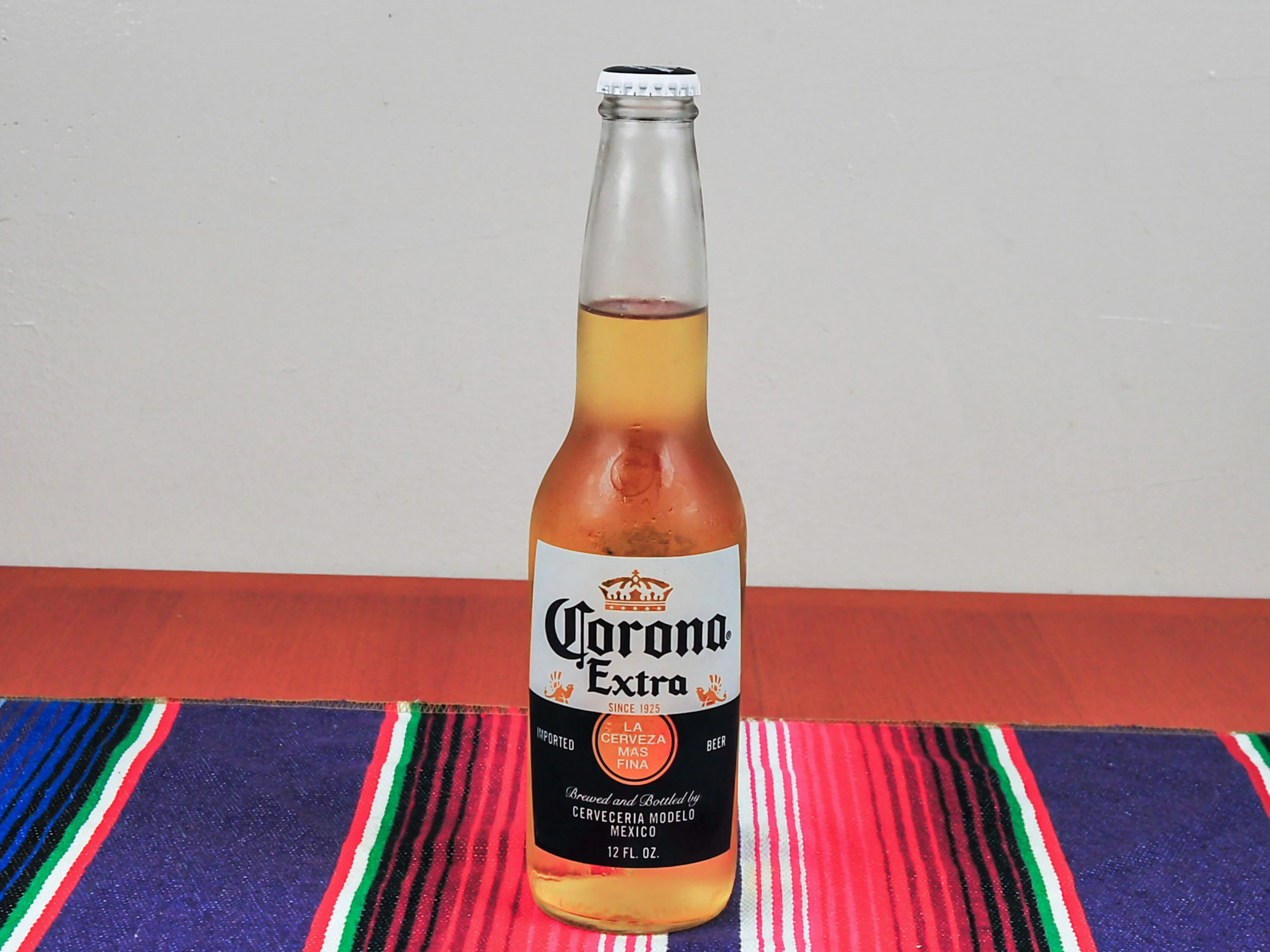 A bottle of light beer with a golden color, displayed on a patterned textile.
