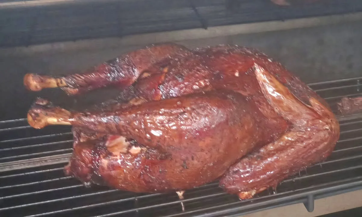 A smoked turkey resting on a grill, showcasing its dark, caramelized skin and juicy appearance.