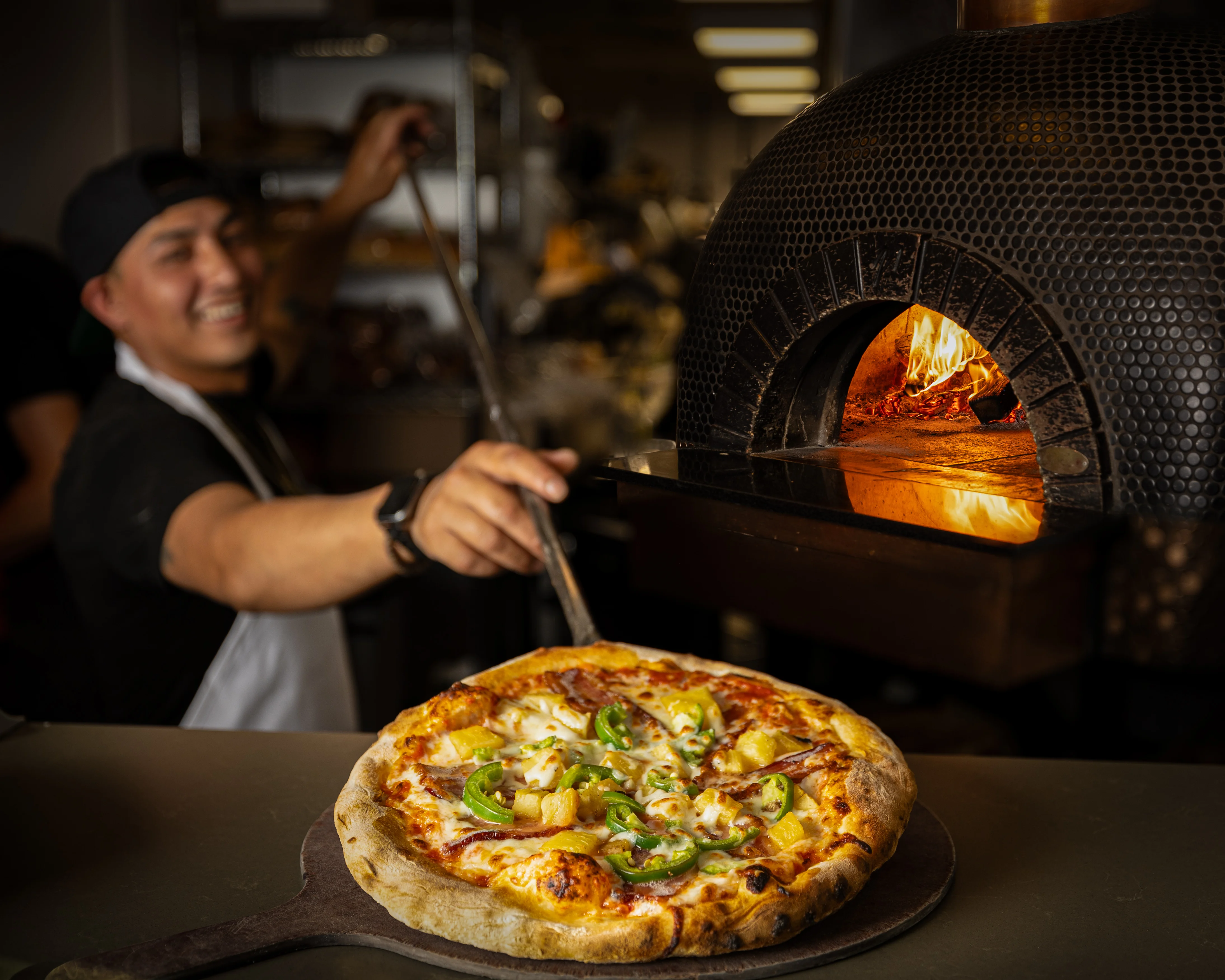 Chef pulling a freshly baked pizza from a wood-fired oven.