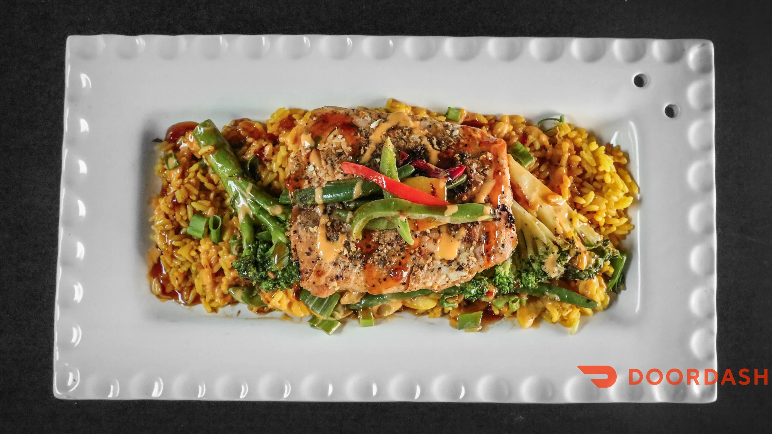 A beautifully plated salmon dish served on a bed of seasoned rice with assorted vegetables and garnished with colorful peppers.