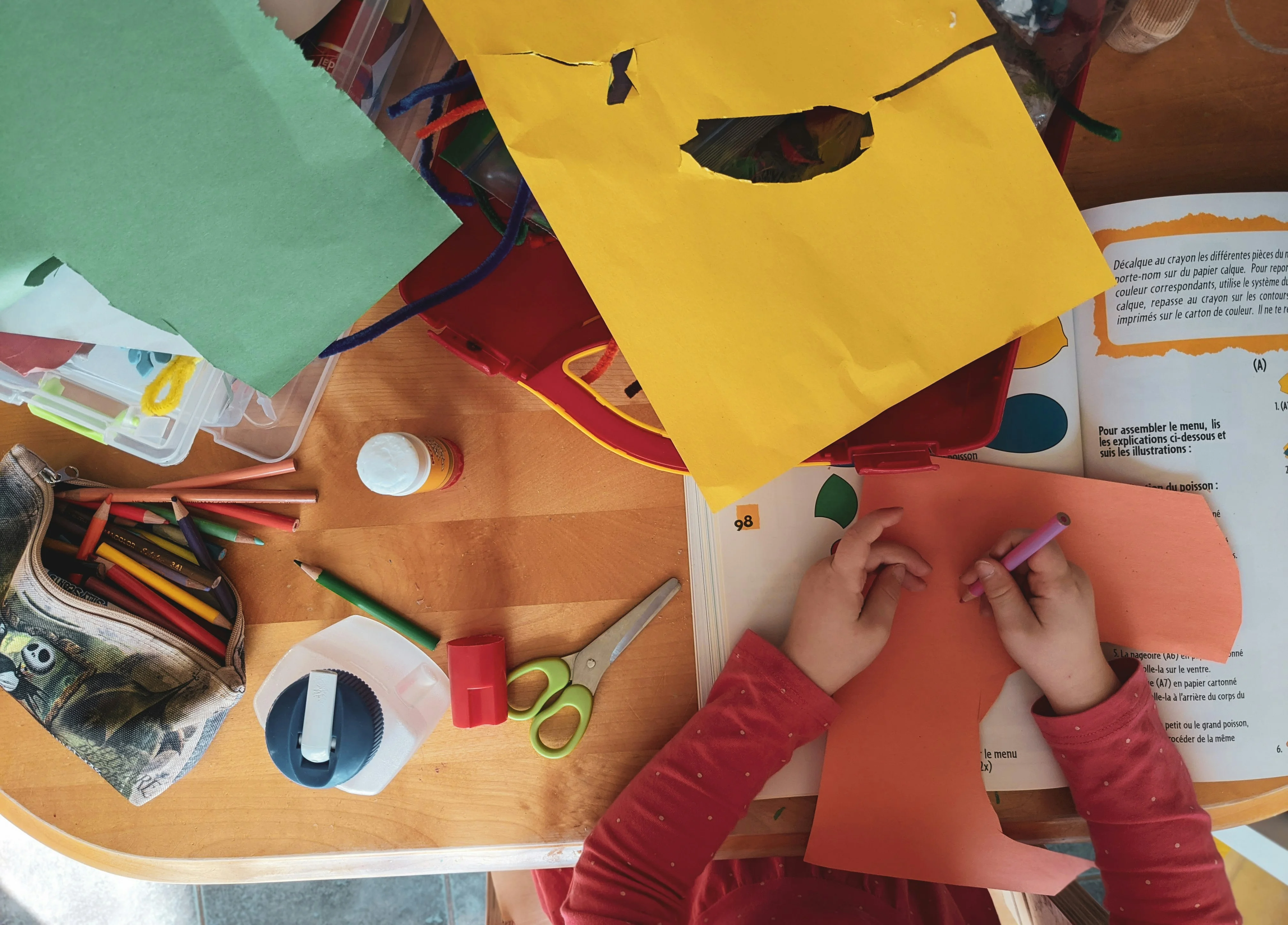 Child crafting with colorful paper and art supplies on a wooden table