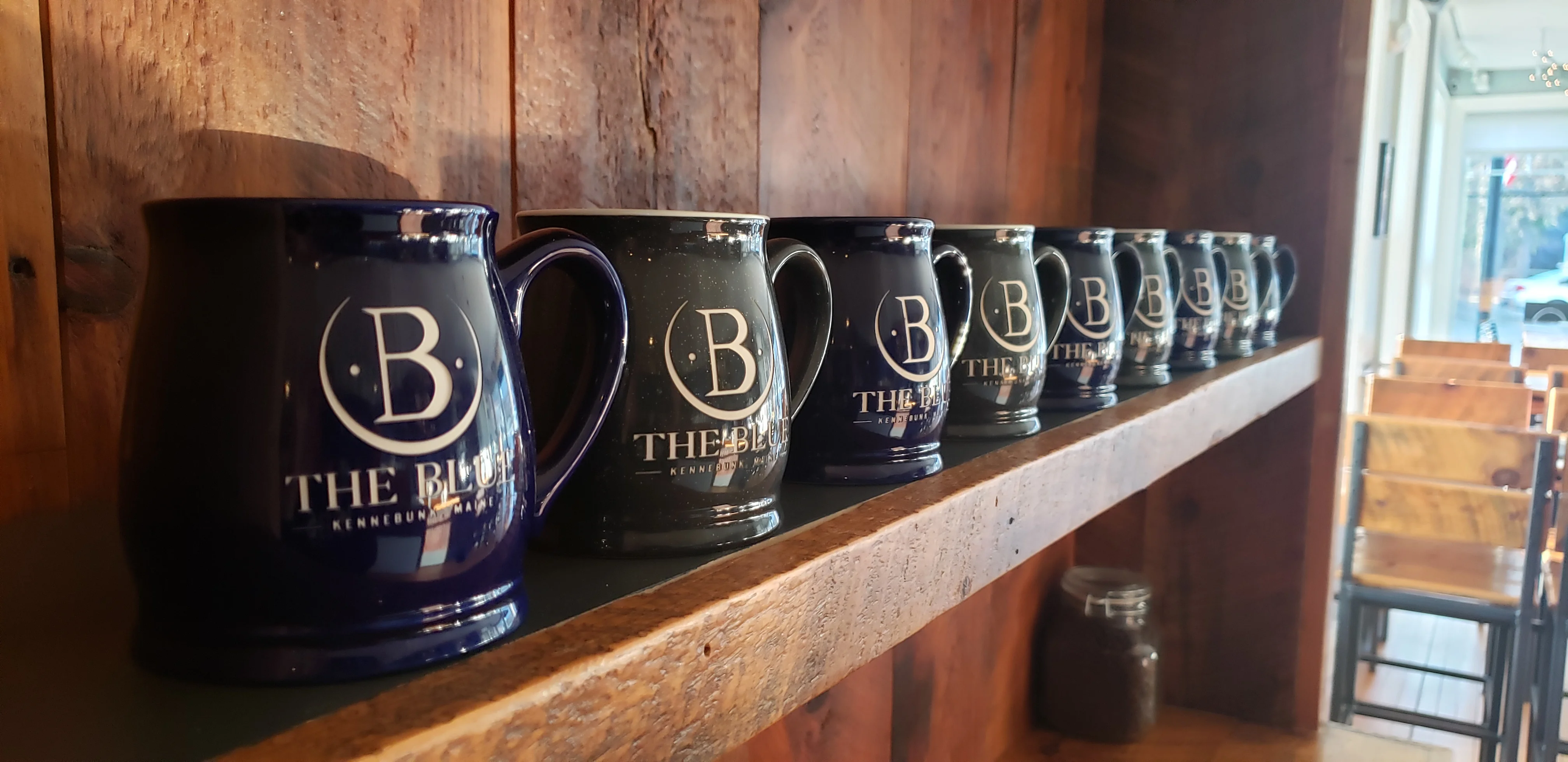 Collection of branded mugs displayed on a wooden shelf in a cozy café