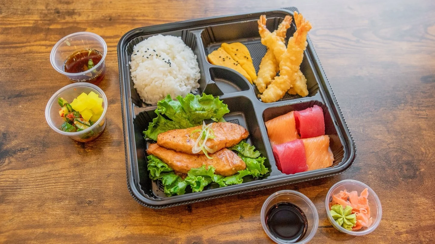 Japanese bento box with sushi, tempura shrimp, salmon, rice, and pickles