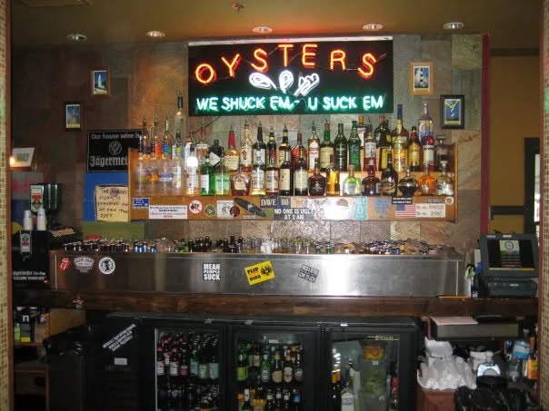 Vibrant bar with a variety of spirits and neon oyster sign