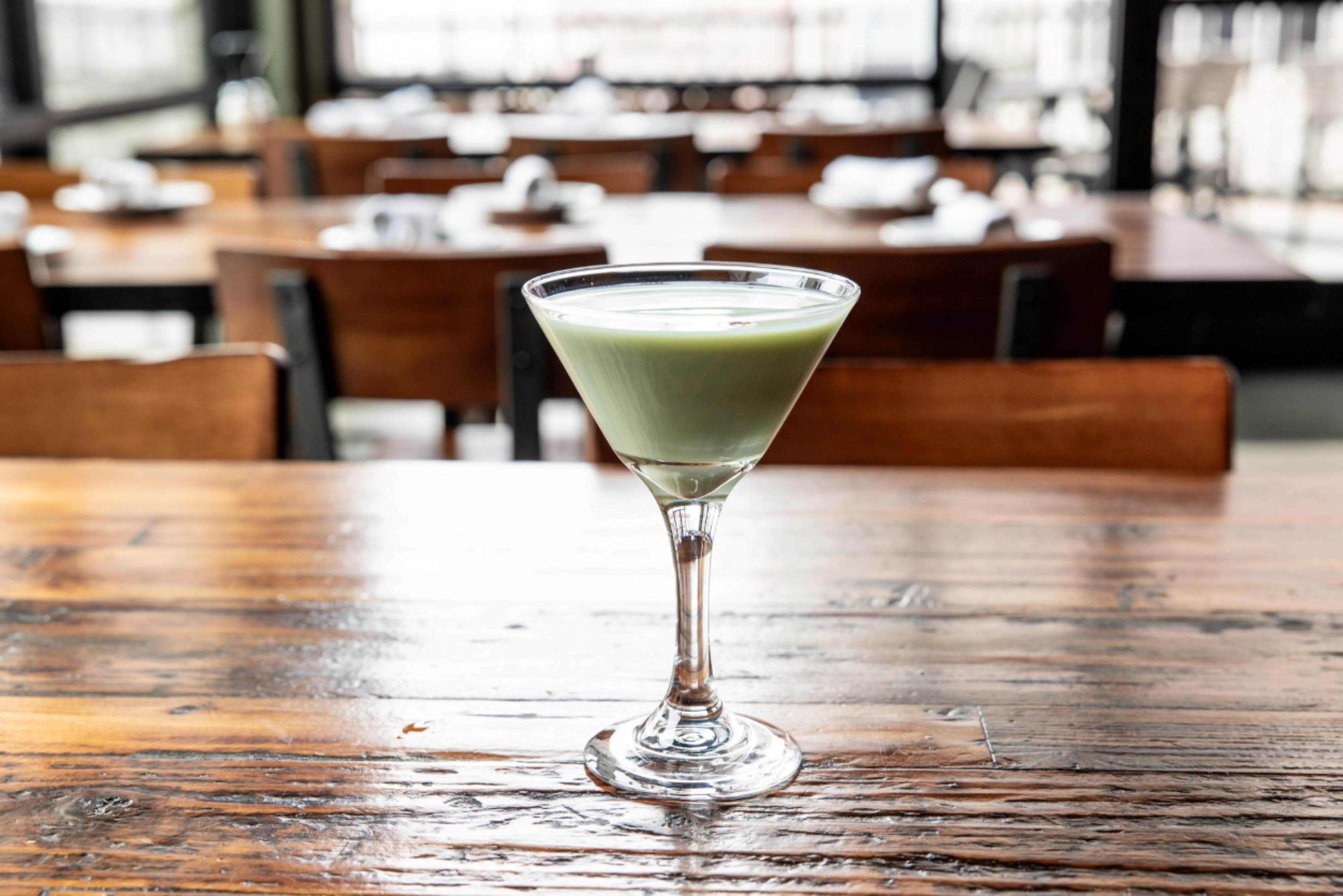 A vibrant pistachio martini garnished with a pistachio on the rim.