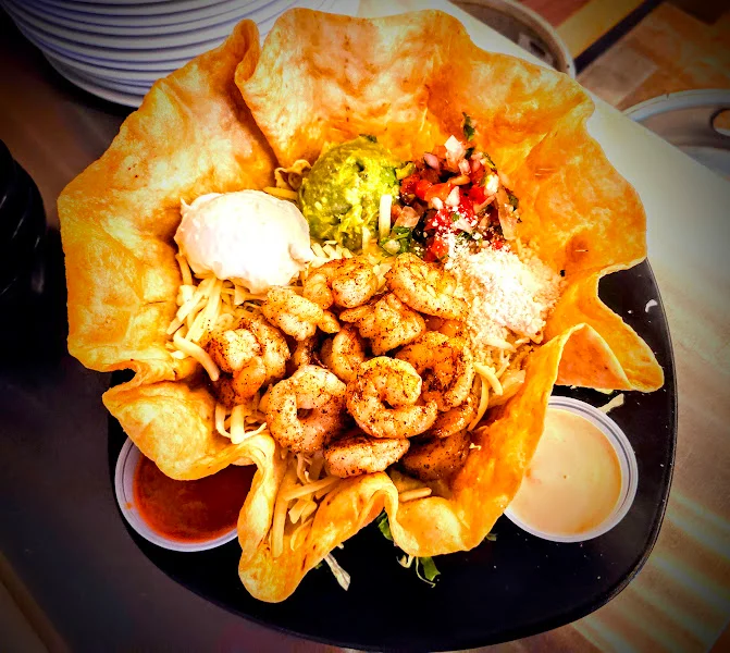 A delicious shrimp salad served in a crispy tortilla bowl, topped with guacamole, sour cream, and fresh pico de gallo.