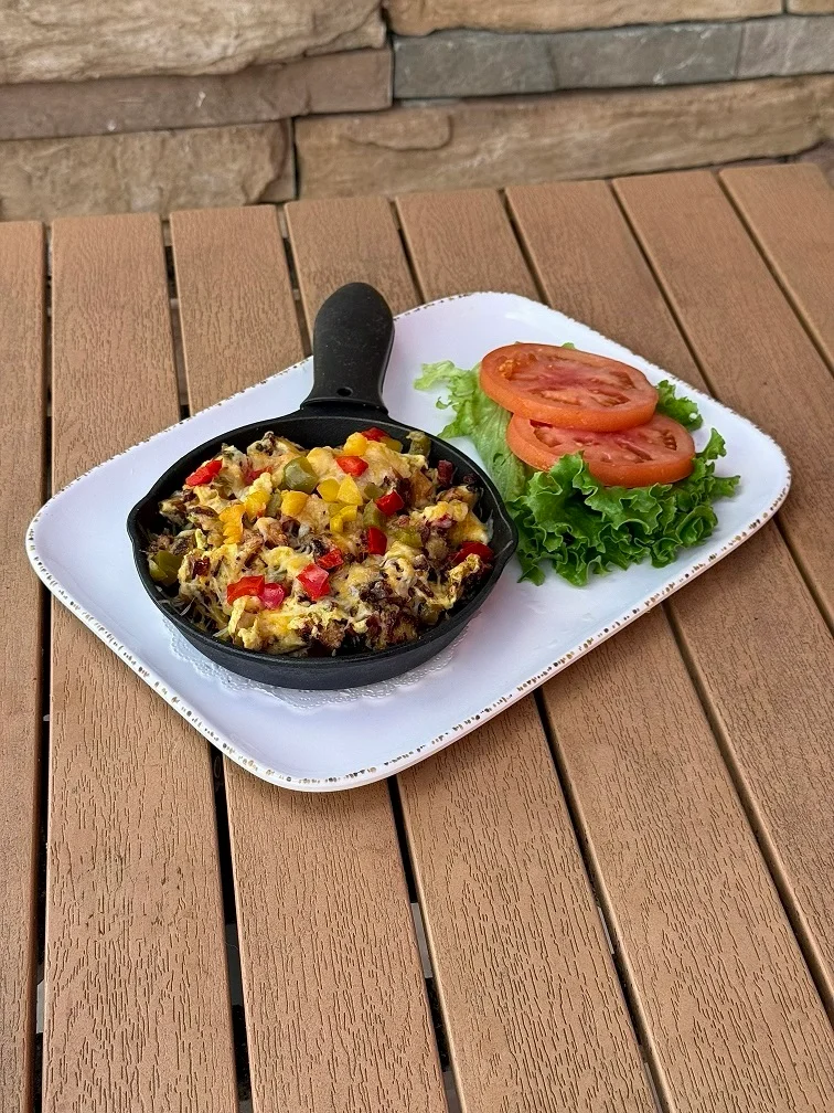 Cast iron skillet with a colorful vegetable and cheese dish, served with lettuce and tomato.