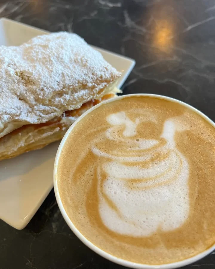 Flaky pastry with powdered sugar and latte art in a cozy café
