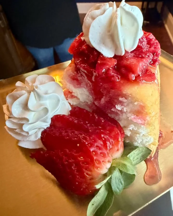 A slice of cake topped with strawberries and whipped cream, served elegantly on a golden plate.