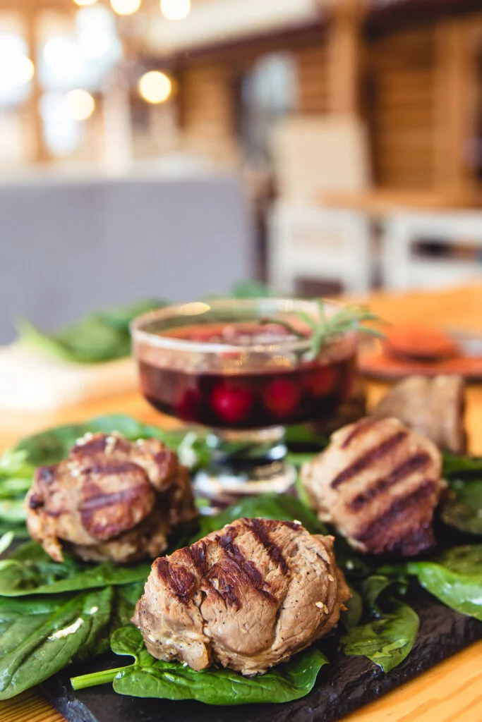 Grilled meat patties served on a bed of fresh spinach, accompanied by a glass of garnished drink.