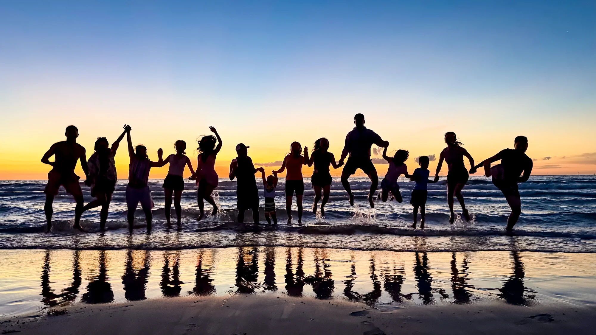 Silhouetted group of people jumping at sunset on the beach
