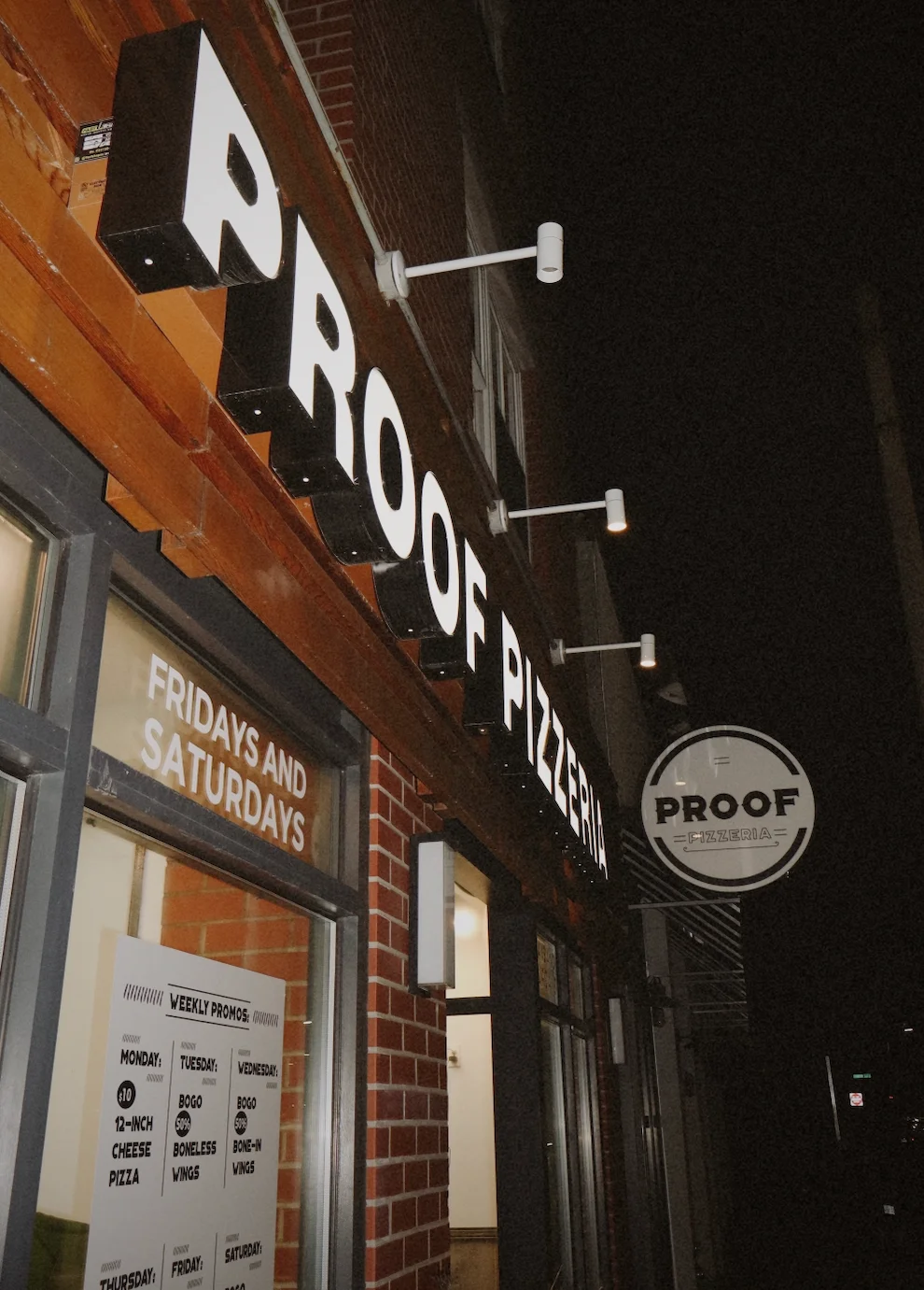 Exterior view of Proof Pizzeria with illuminated signage at night