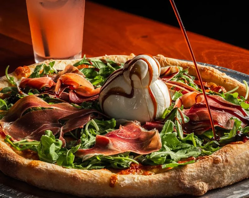 Italian prosciutto pizza topped with arugula and burrata