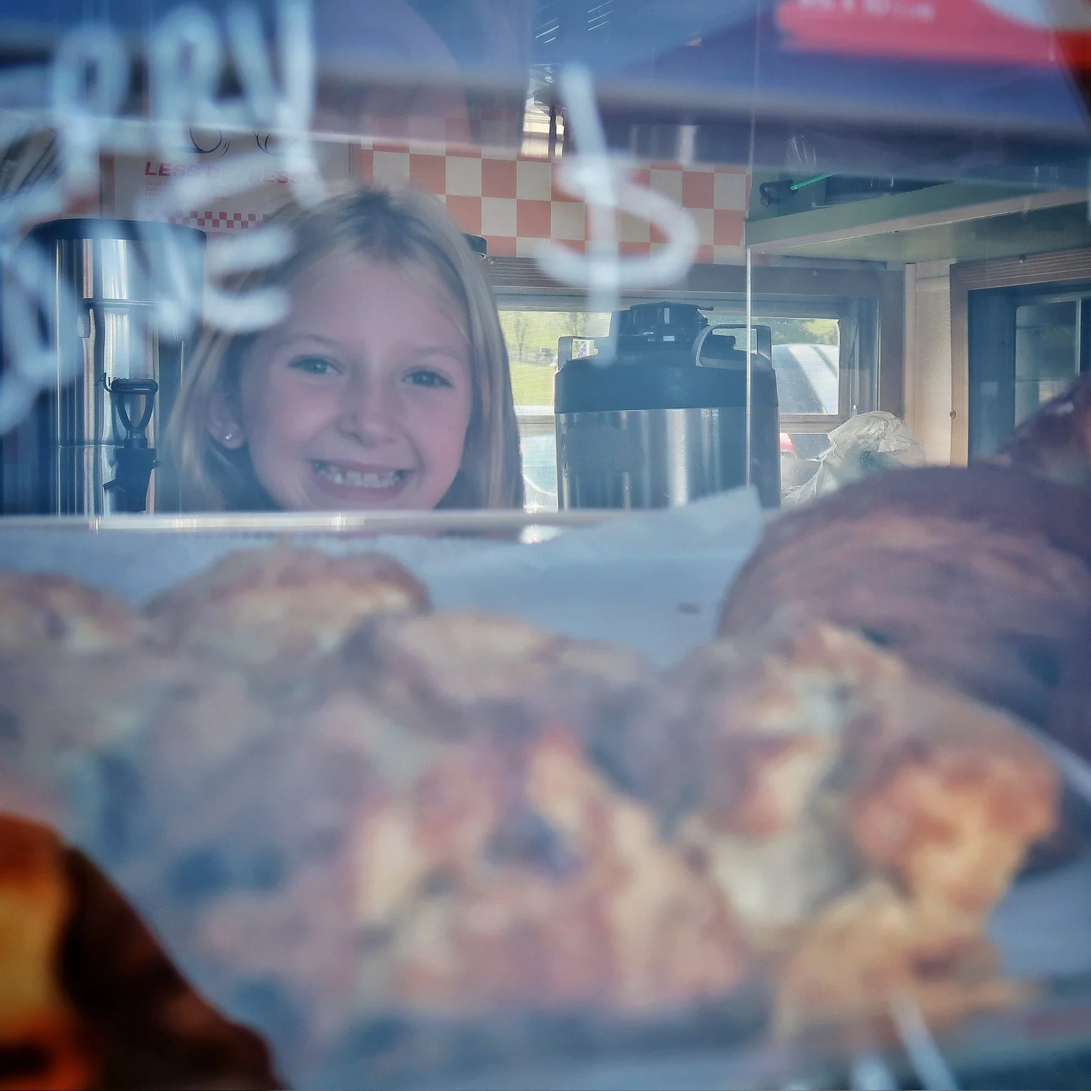 Child smiling behind a bakery display with fresh pastries