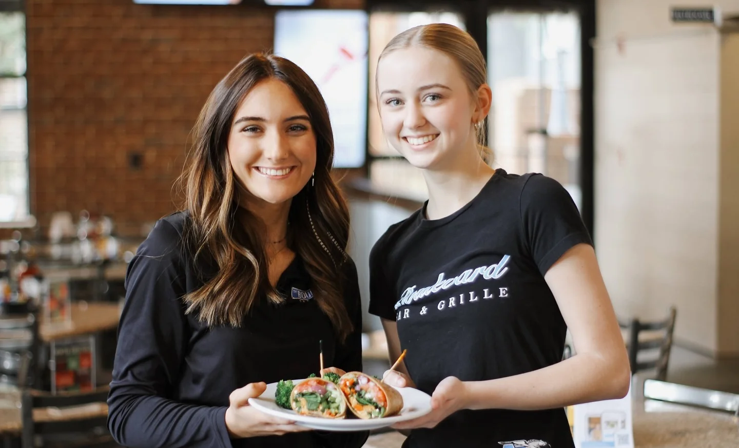 Two servers presenting fresh wraps in a casual dining setting
