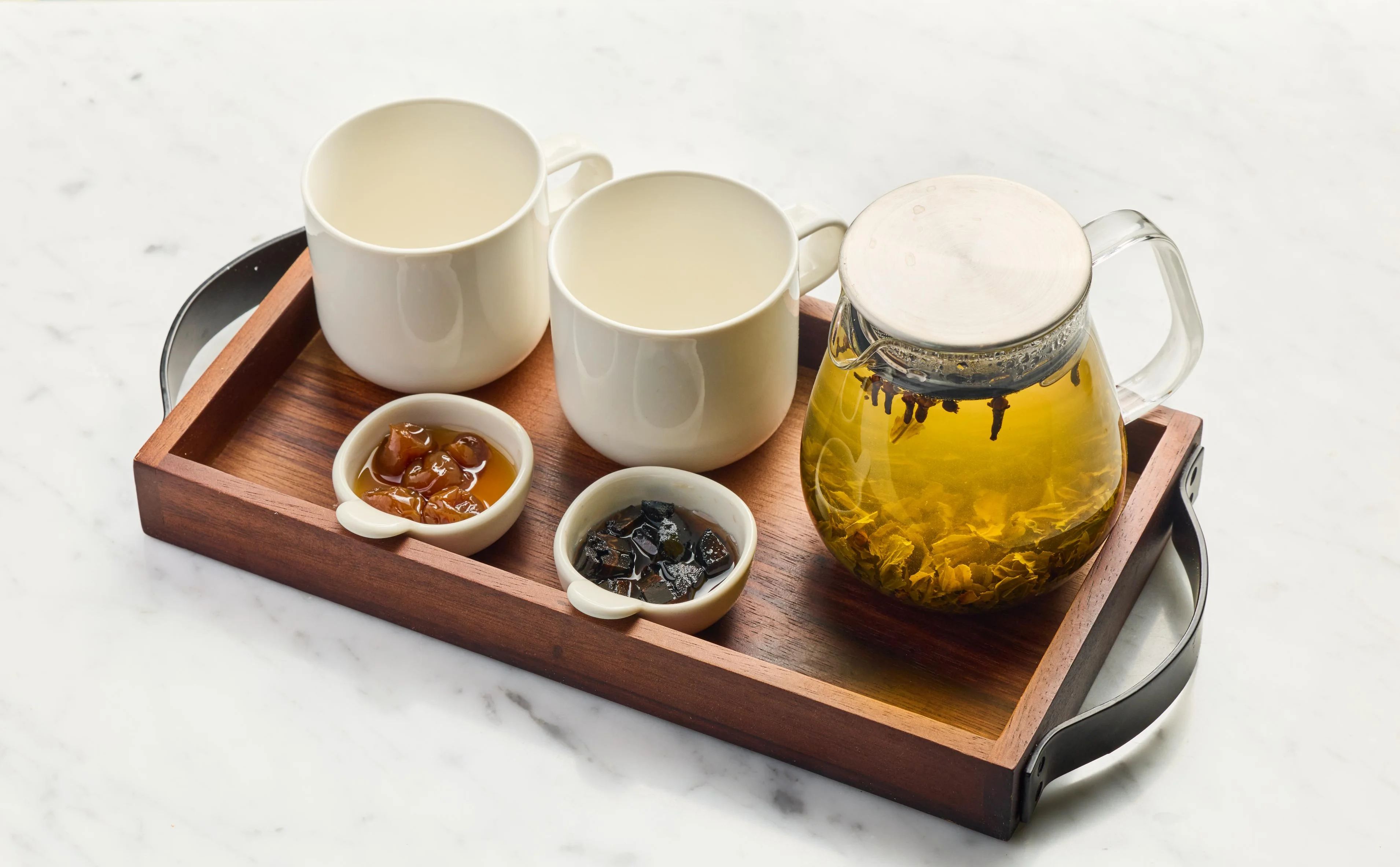 A wooden tray with two cups, a teapot, and two small bowls of condiments.