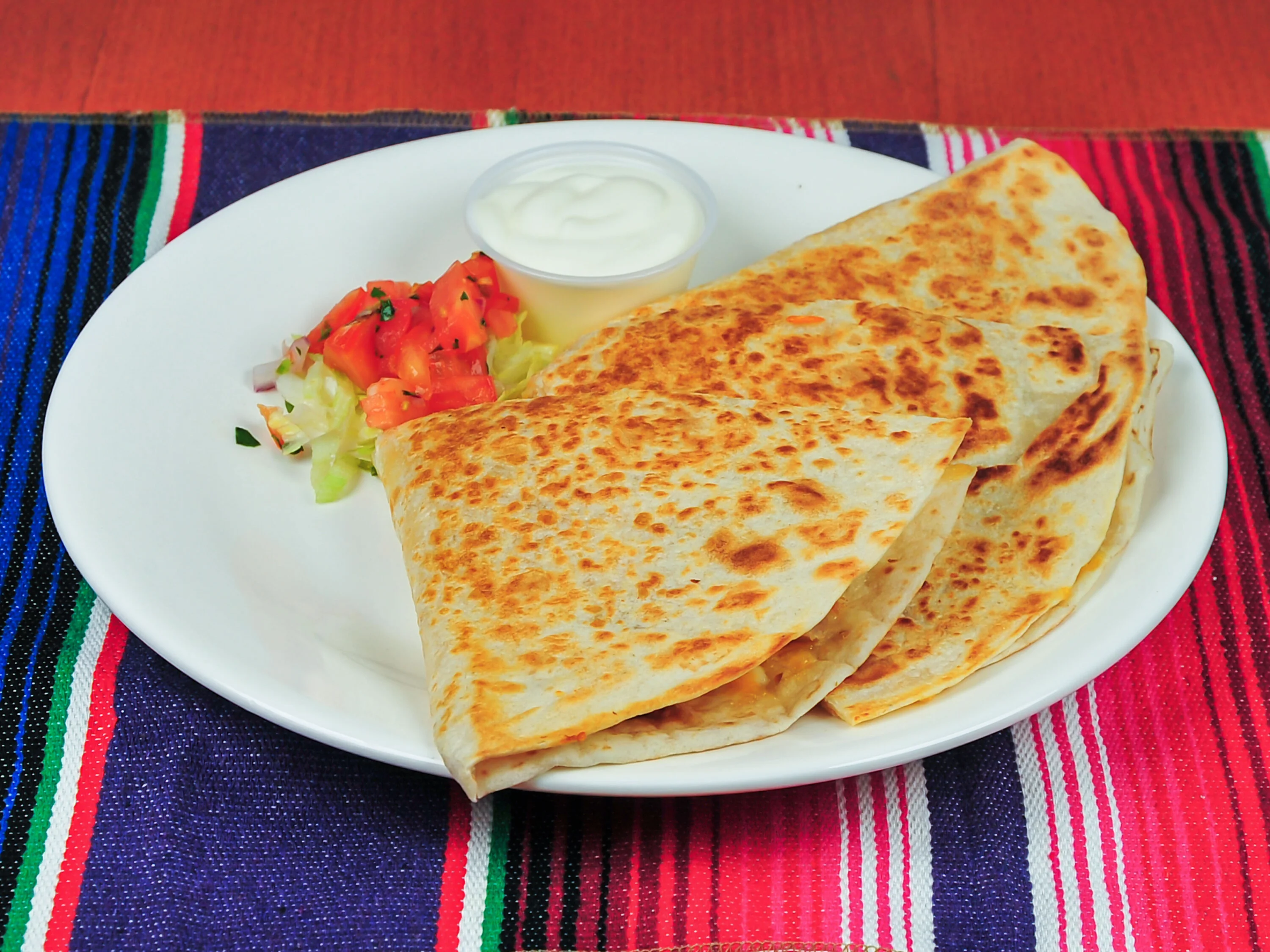 A plate with several golden-brown quesadillas, accompanied by a small bowl of sour cream and a side of salad with diced tomatoes.