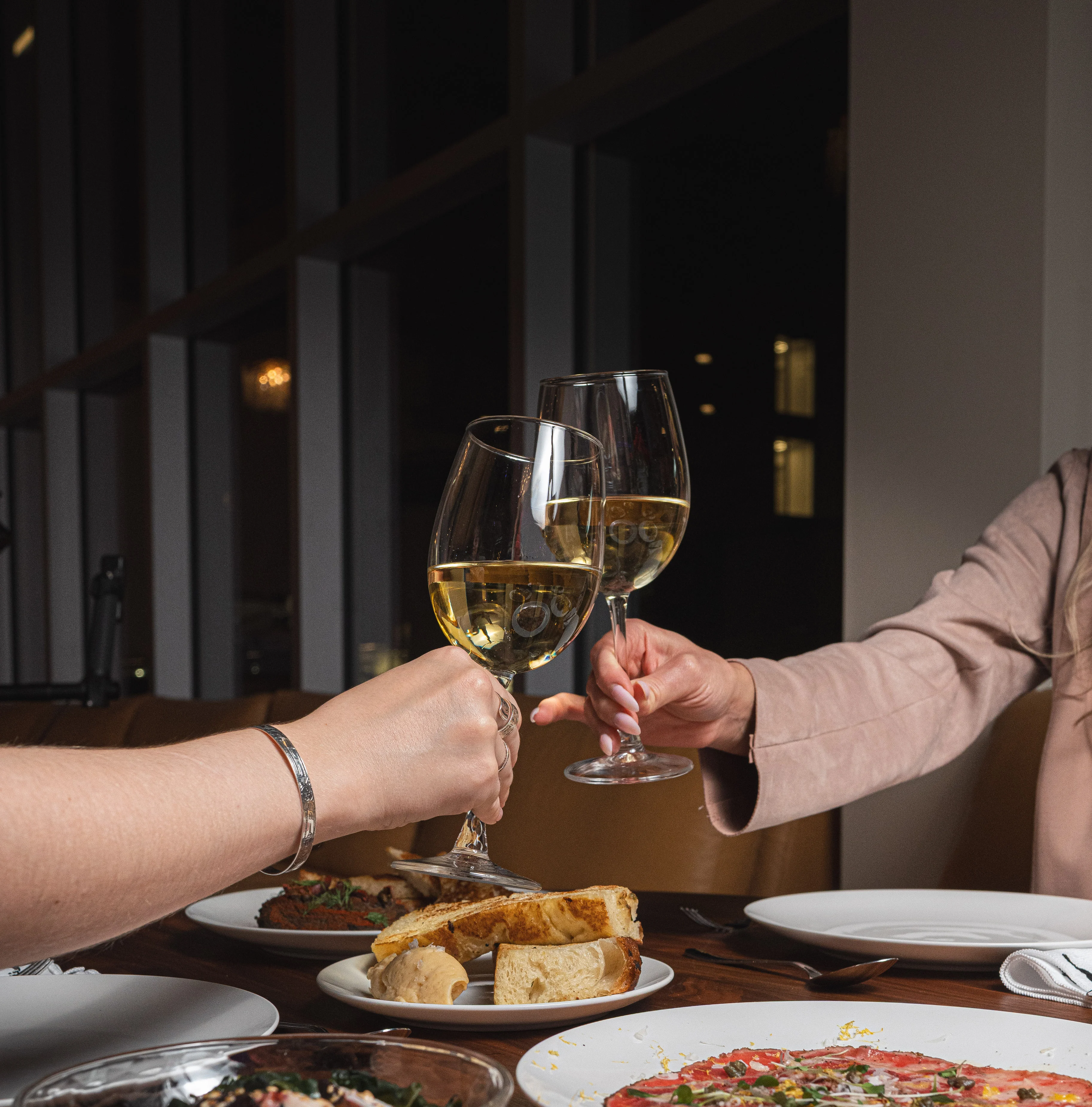 Cheers with white wine glasses at a dining table with various dishes