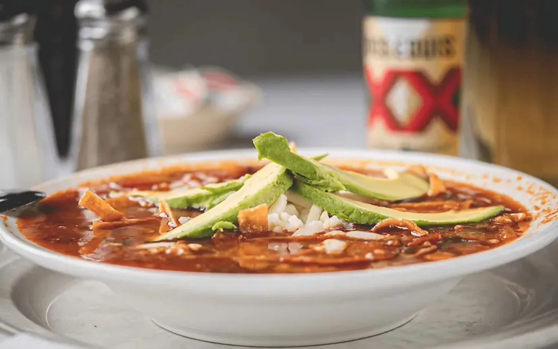 Bowl of Mexican pozole topped with avocado and tortilla strips