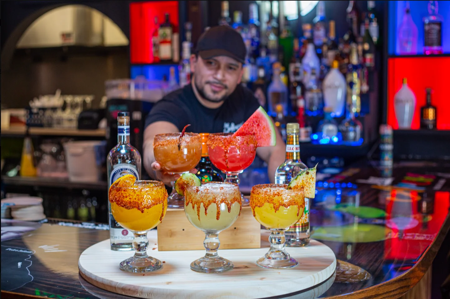 Bartender showcasing colorful cocktails at a vibrant bar