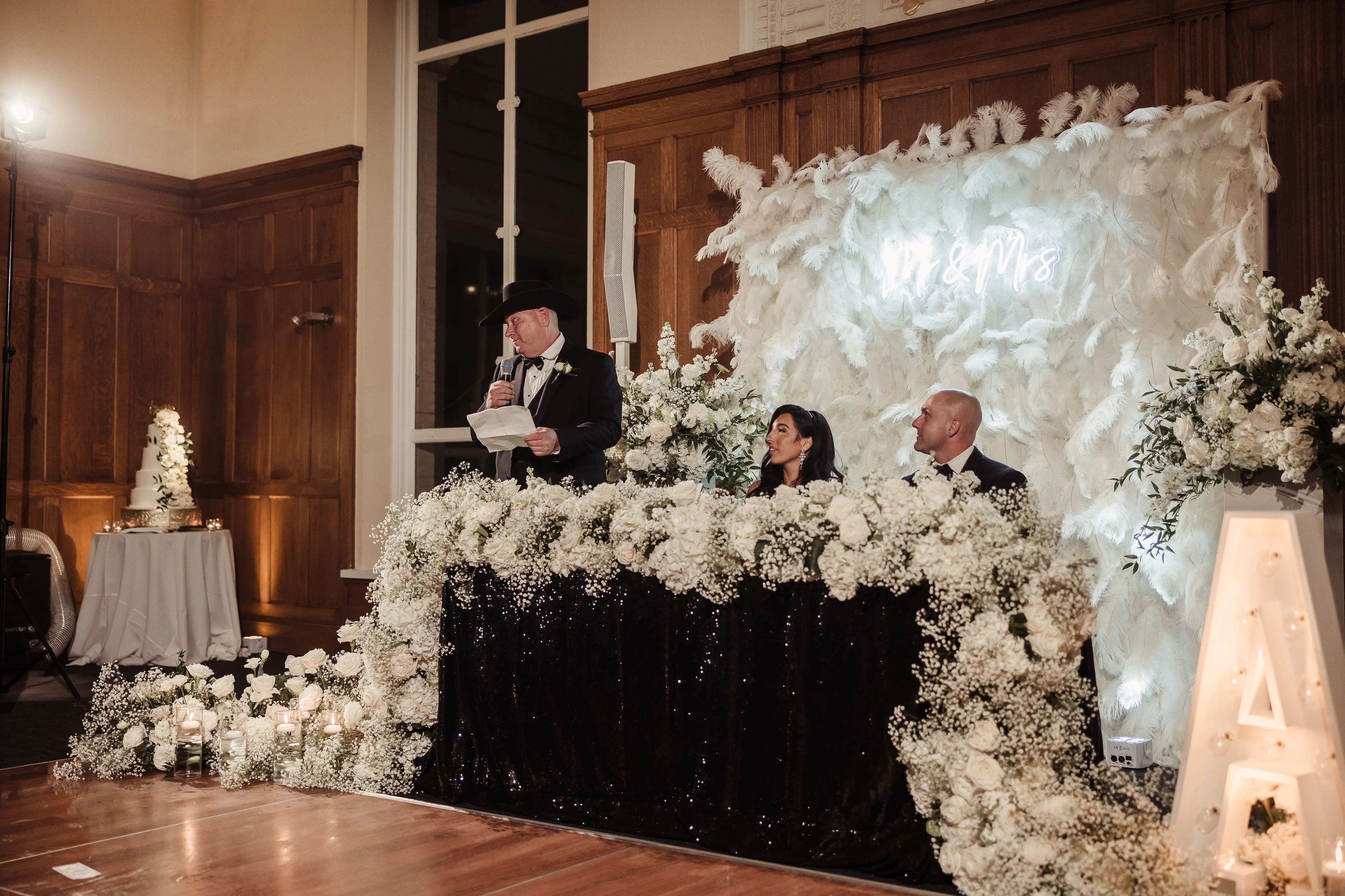 Elegant wedding reception with floral decor and a speaker at the head table