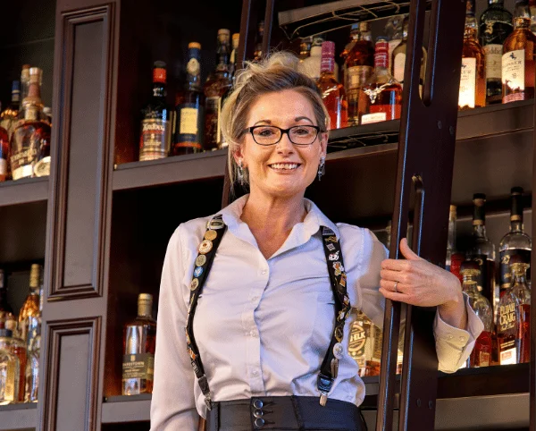 Bartender smiling in front of a well-stocked liquor shelf