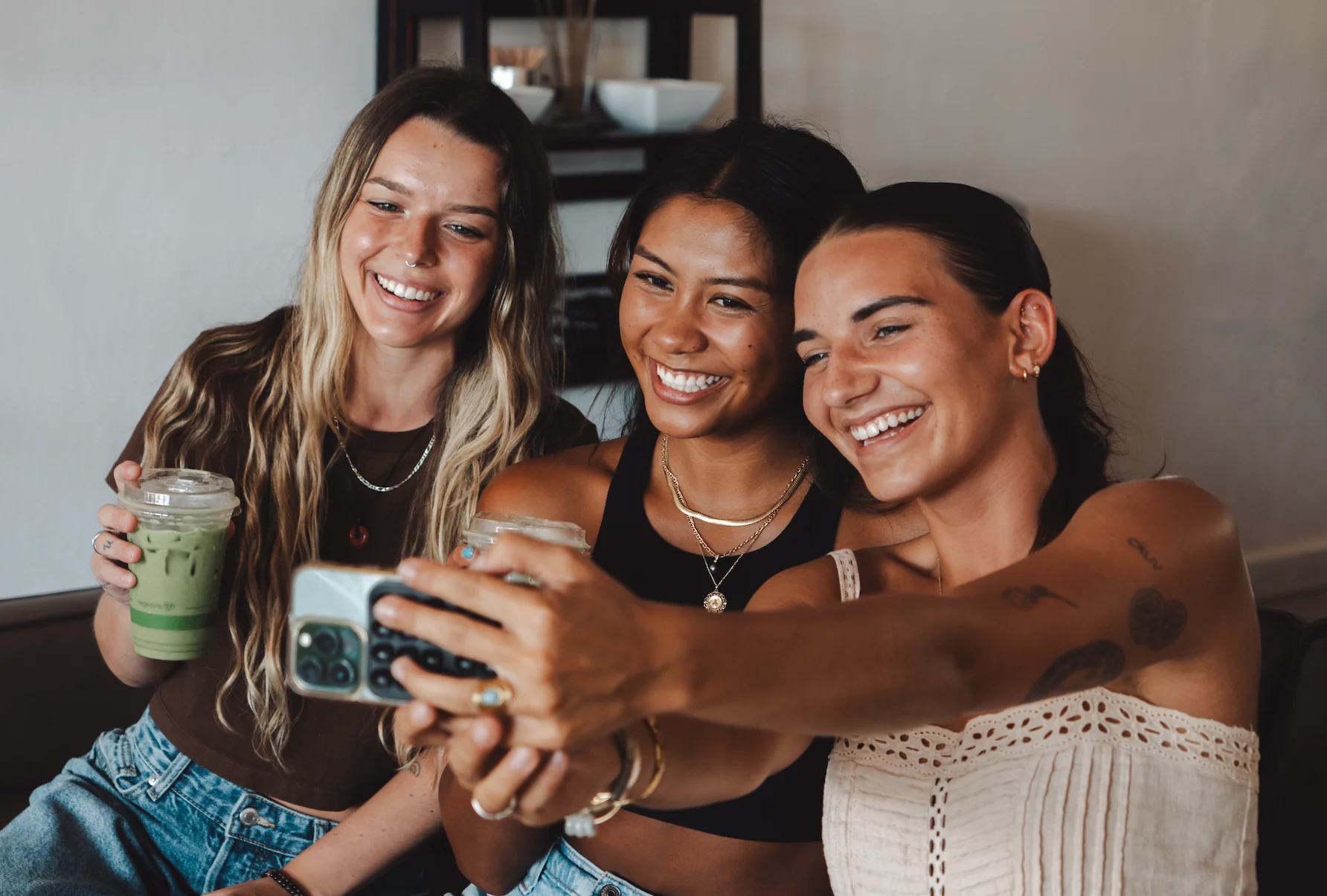 Three friends enjoying drinks and taking selfies in a cozy cafe