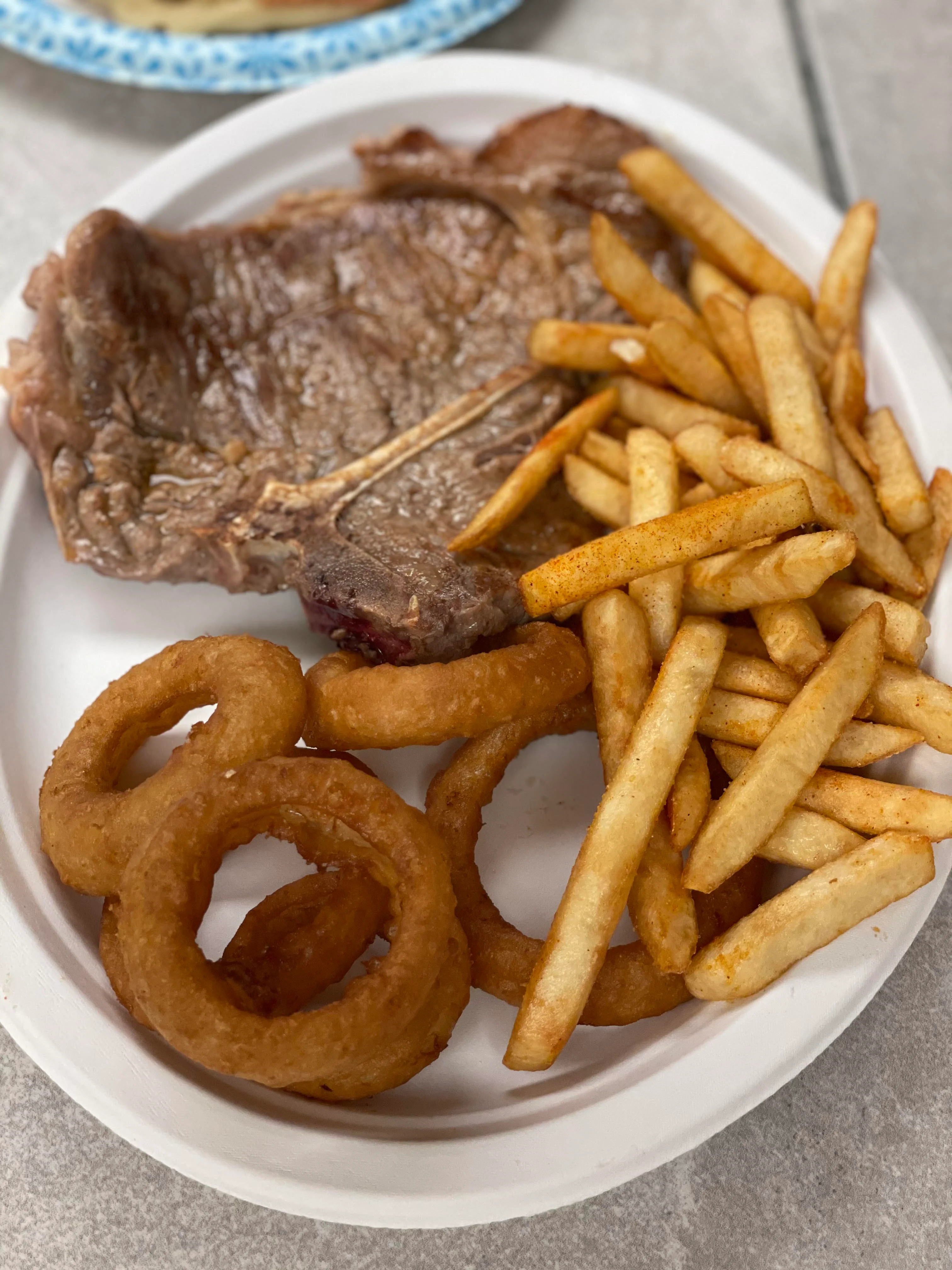 Grilled steak with fries and onion rings on a white plate