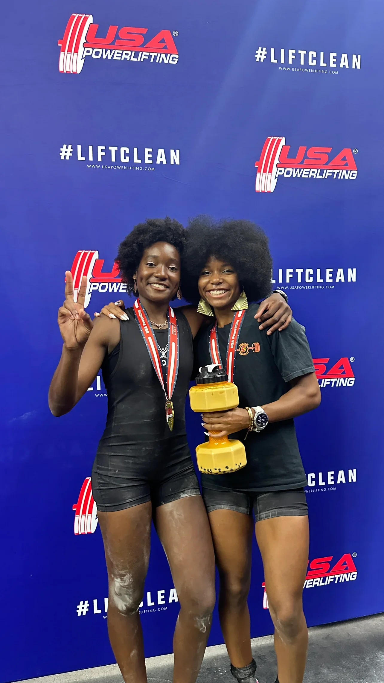 Two powerlifters celebrating with medals at a USA Powerlifting event