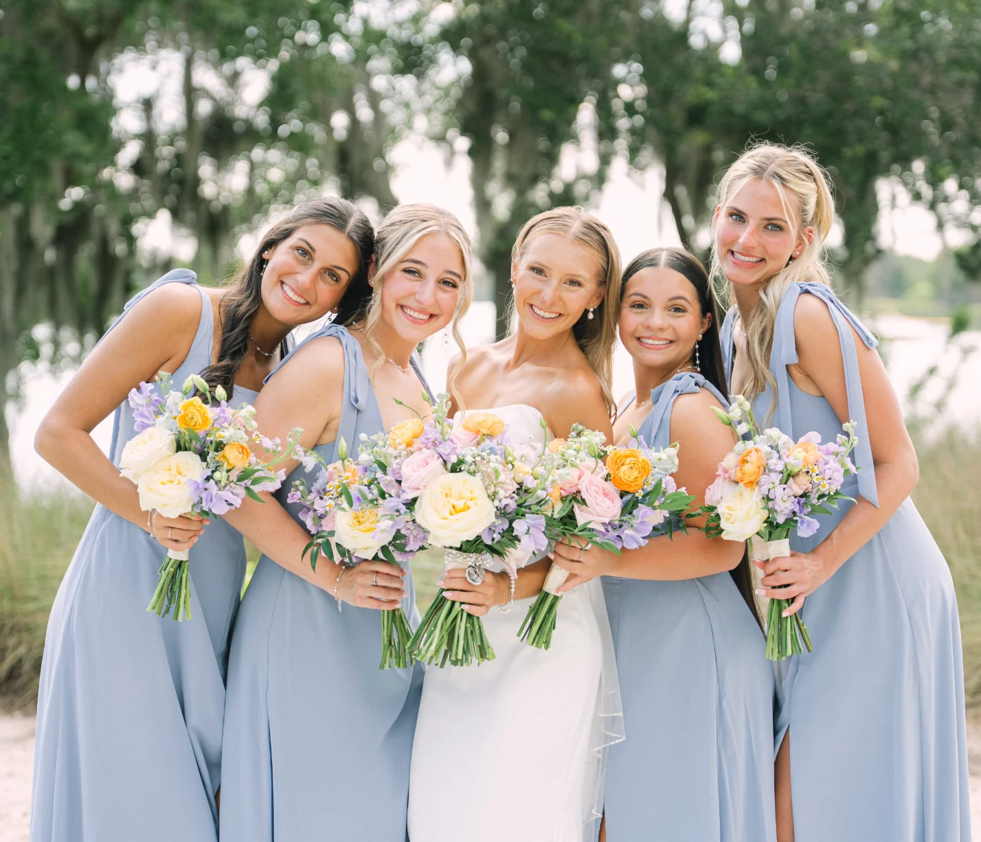 Bridesmaids in blue dresses holding colorful bouquets