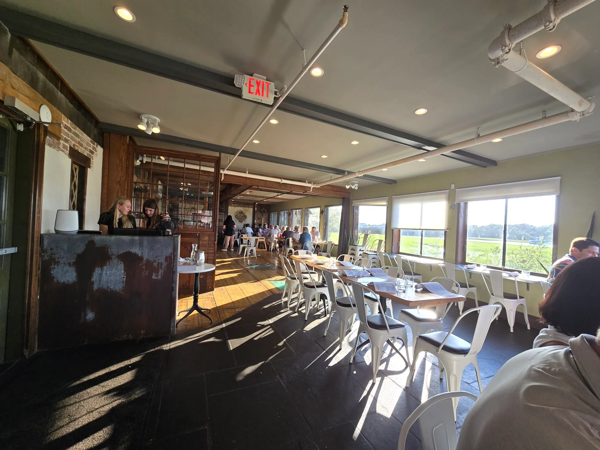 Indoor dining room at The Mill Street Tavern with tall windows looking out over the Shem Creek marsh