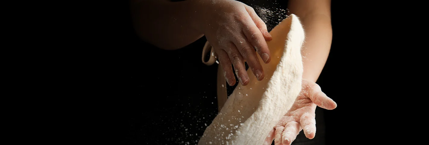 Chef tossing pizza dough in a dark kitchen