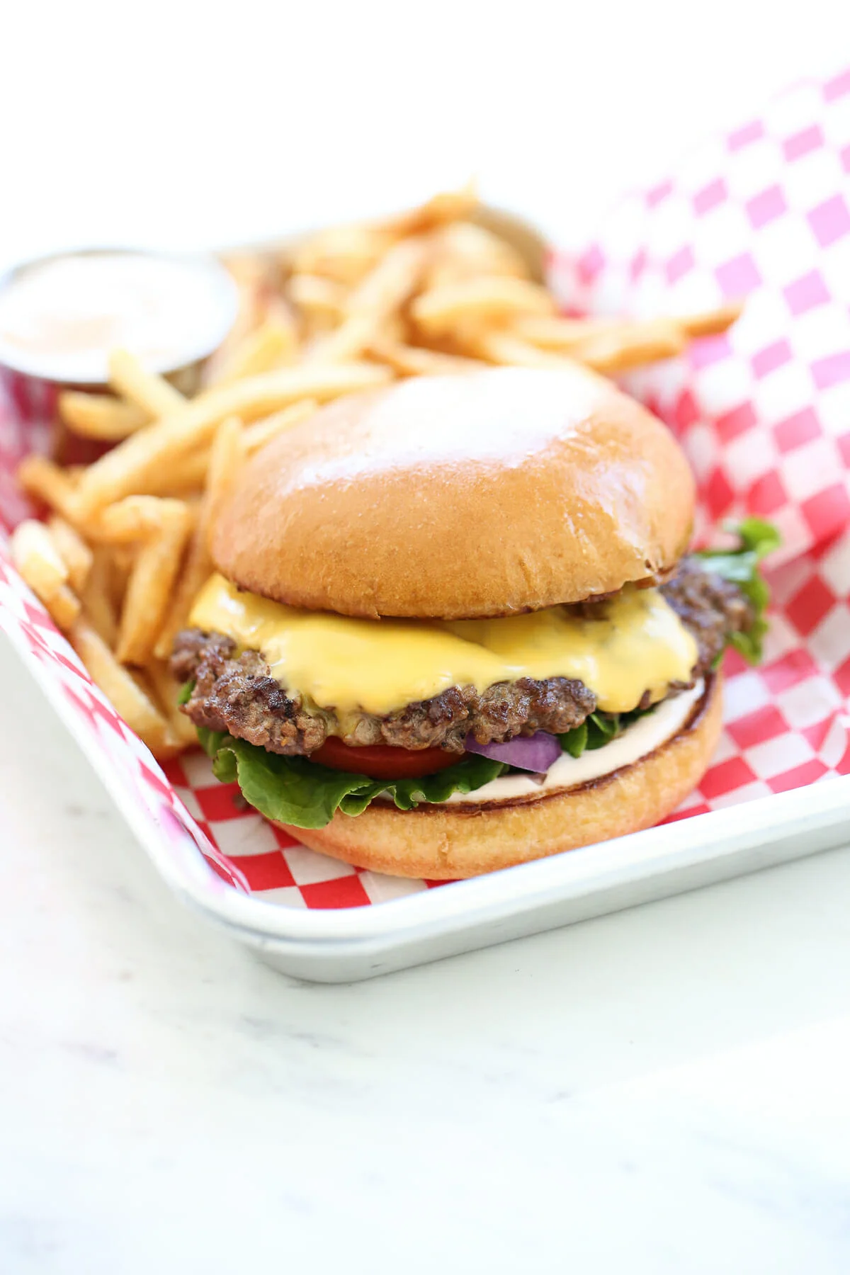 A juicy cheeseburger served with lettuce, tomato, and onion on a toasted bun, alongside a side of golden French fries.