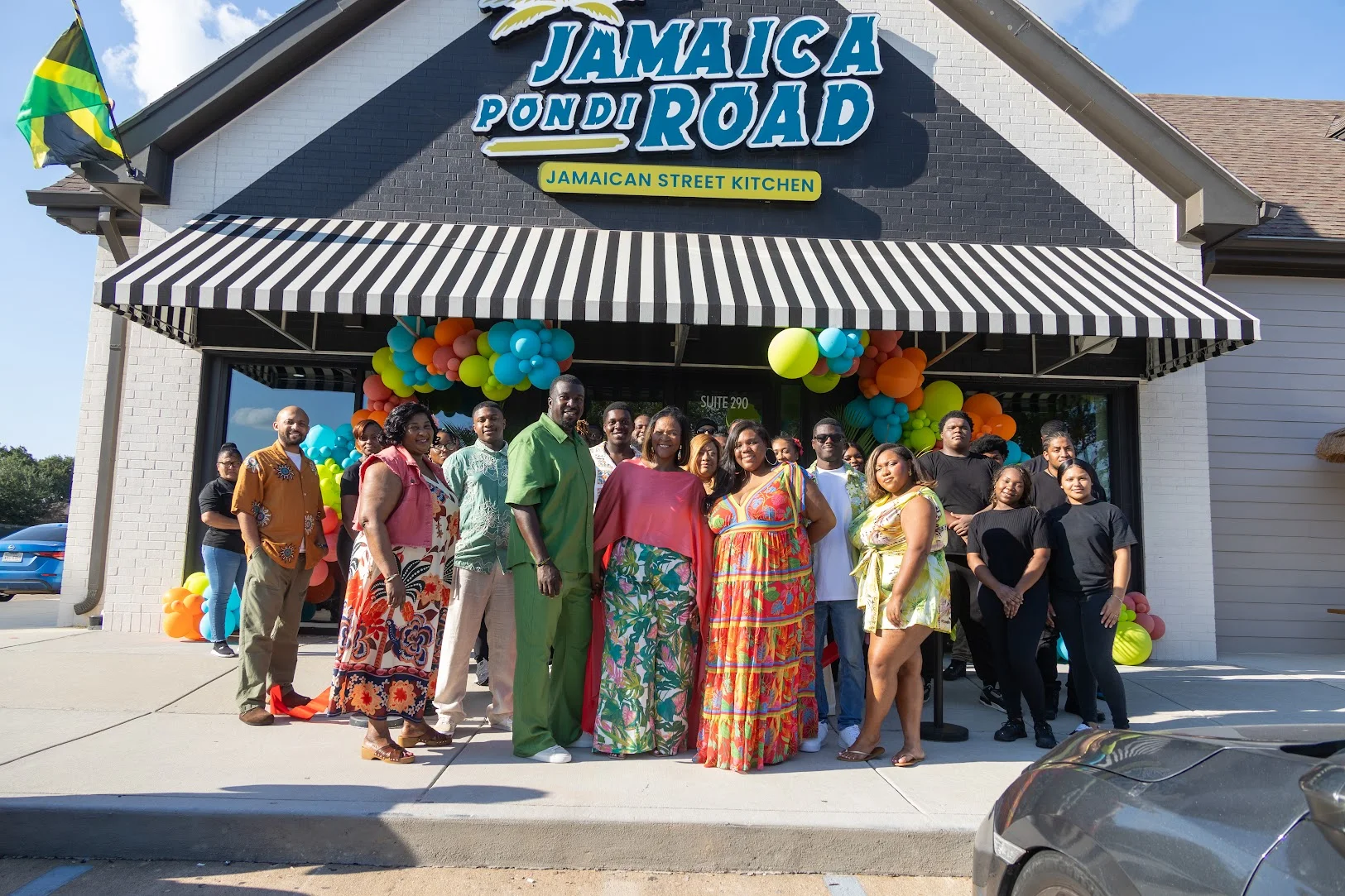 Jamaican restaurant exterior with colorful balloons and a celebratory group photo