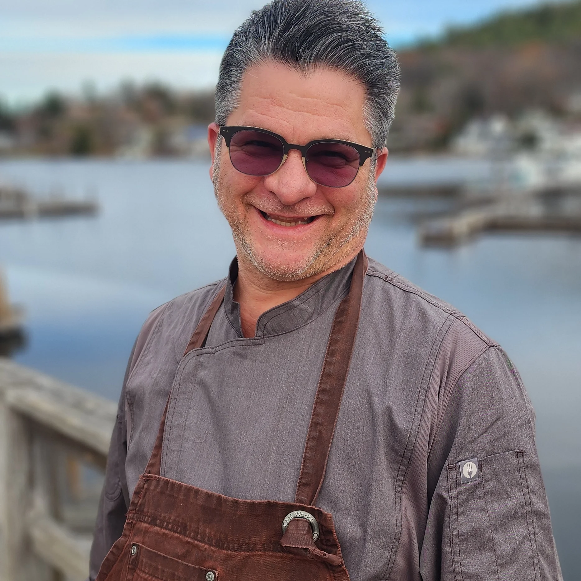 Chef smiling by the waterfront in a rustic apron