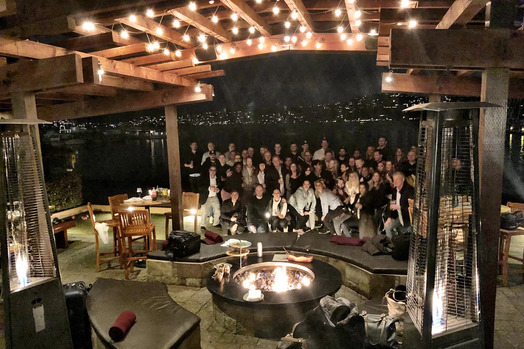 group of friends gathered for a photo around the firepit, overlooking the bay at night