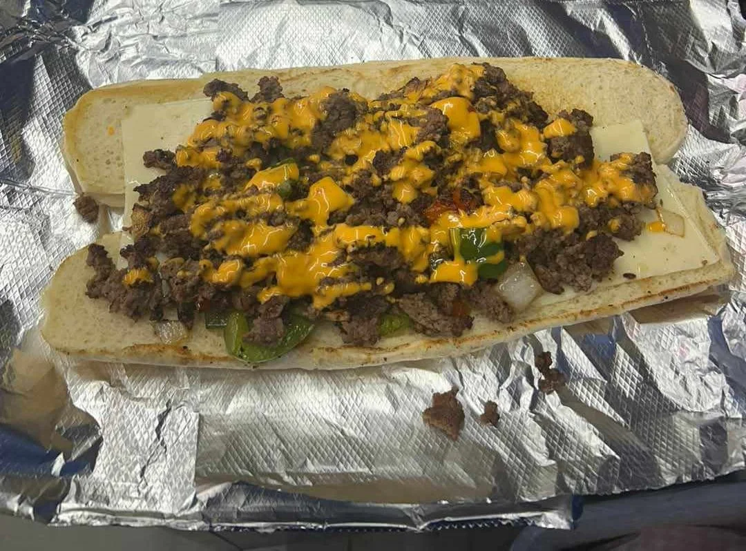 A loaded sandwich with ground beef, melted cheese, and colorful vegetables on a hoagie roll.