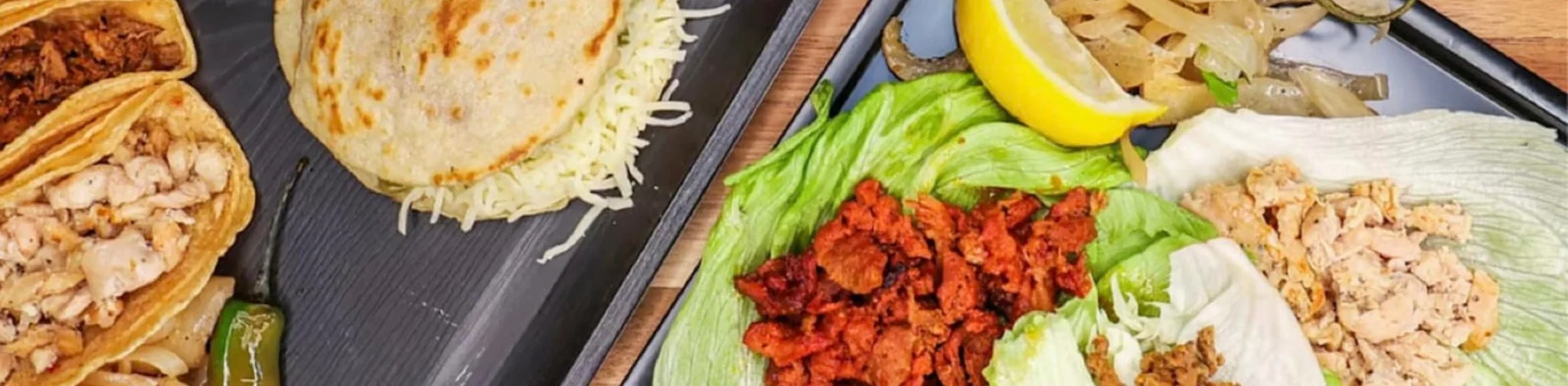Assorted Mexican tacos and pupusas on a wooden table