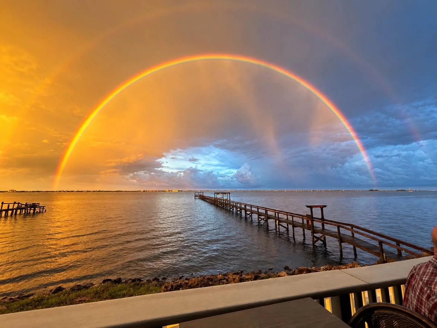 Vibrant sunset over water with a rainbow and wooden pier