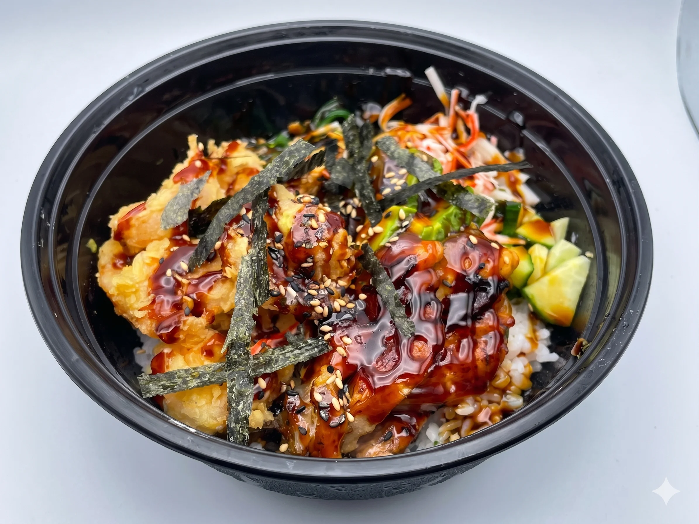 Bowl of sushi with tempura, rice, vegetables, and sauce.