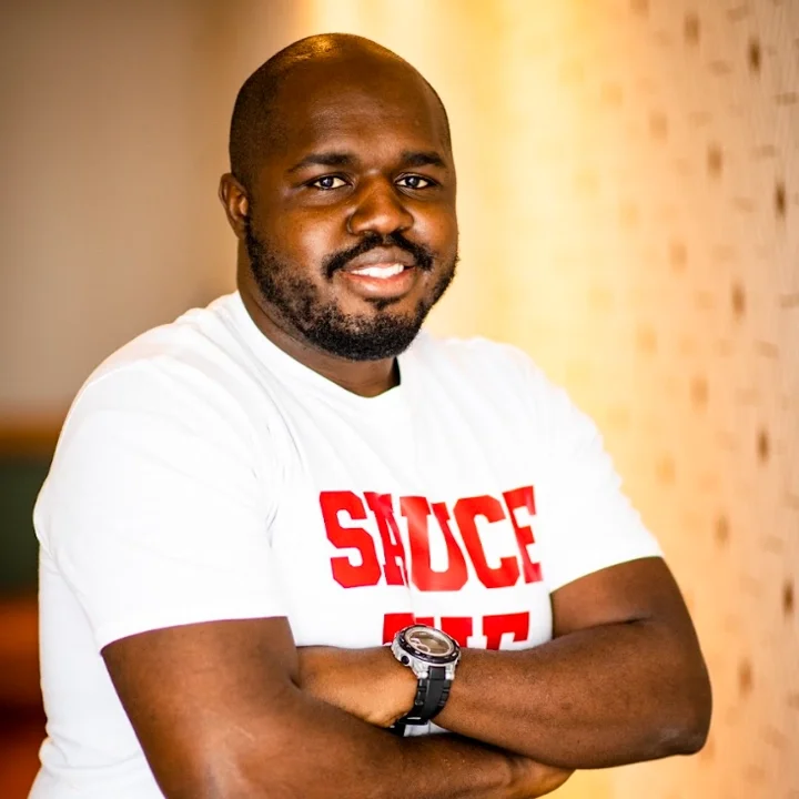 Smiling man in a white shirt with red lettering, arms crossed