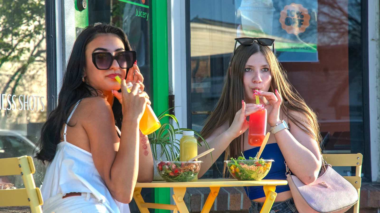 Two friends enjoying fresh salads and juices at a vibrant outdoor café