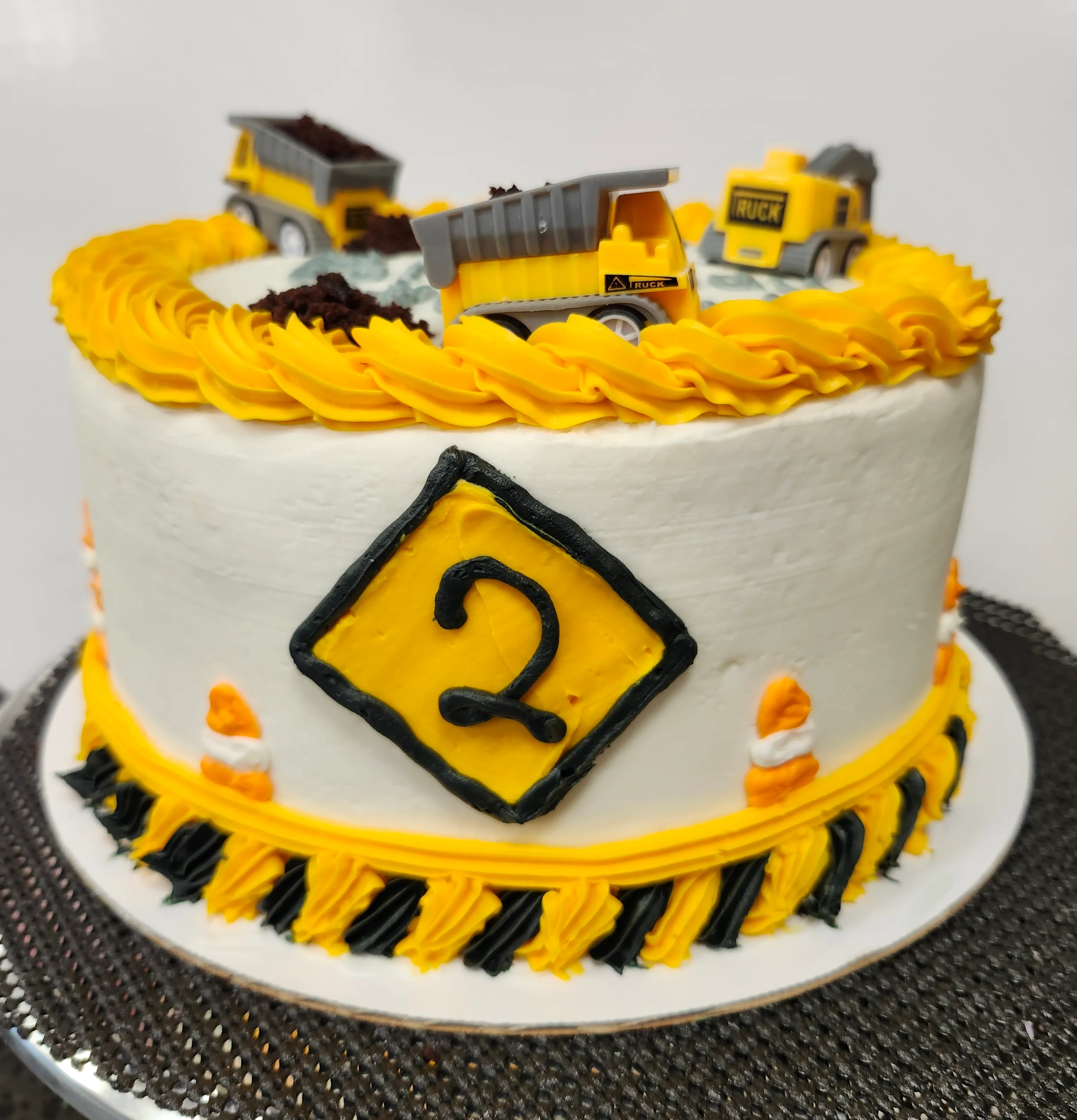 Round cake decorated with construction cones& tape with various toy trucks on top.