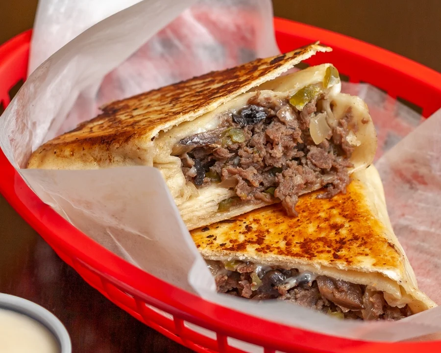 A grilled and toasted flatbread filled with beef and vegetables, cut in half and served in a basket.