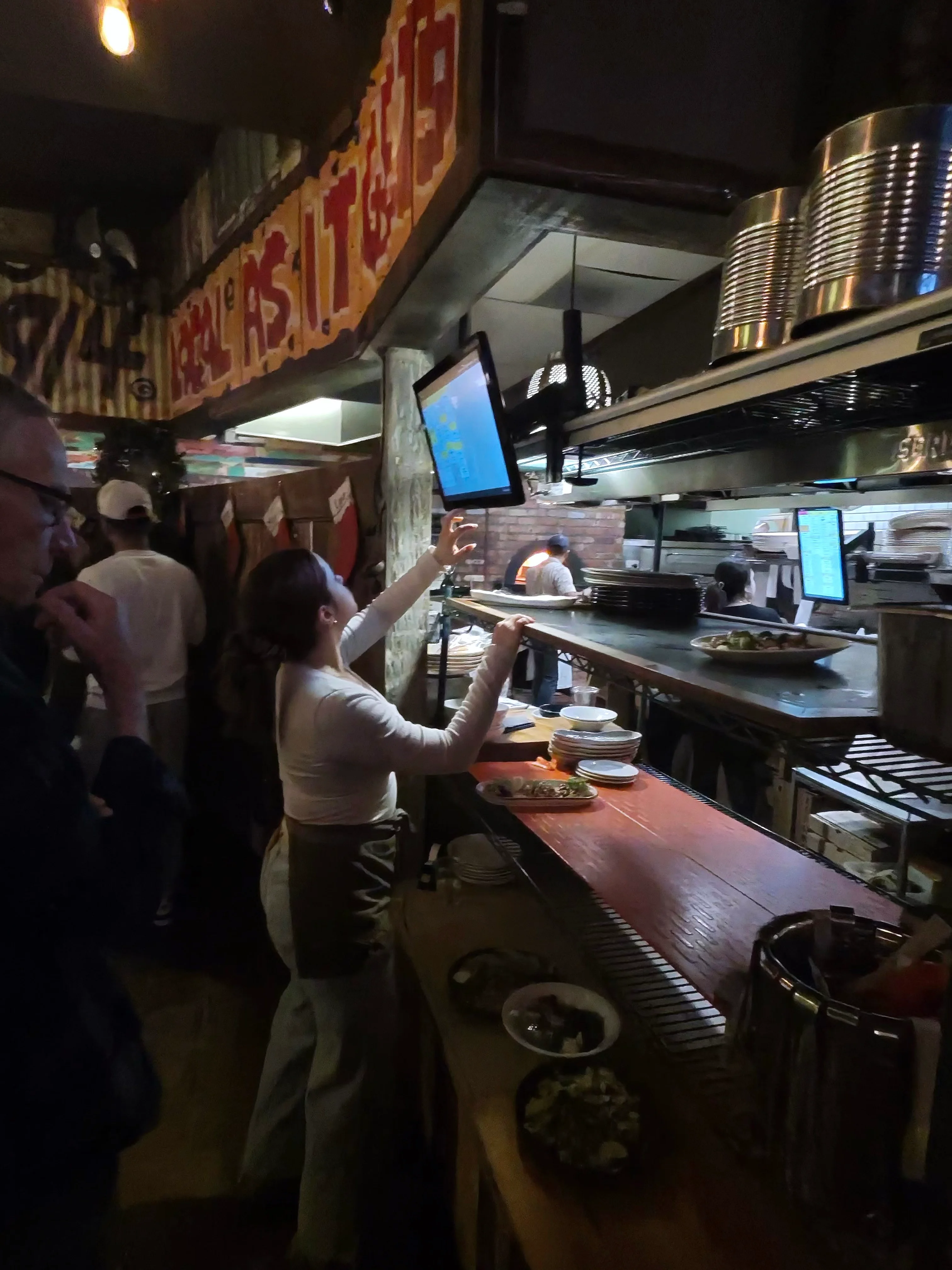Server checking order status at the expo station with the kitchen team working behind them