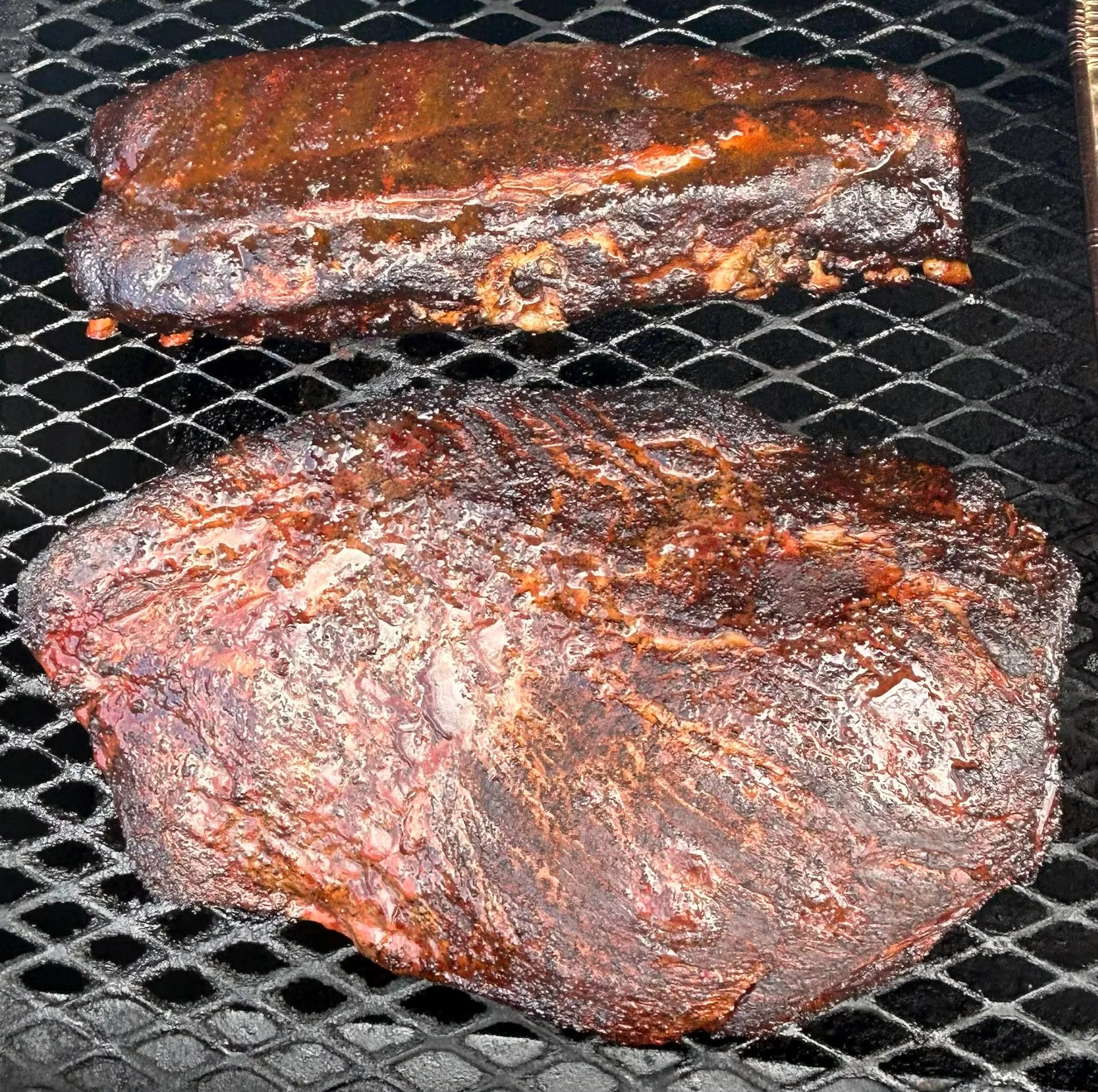 Two pieces of smoked meat on a grill, showcasing a rich, dark exterior with glistening juices.