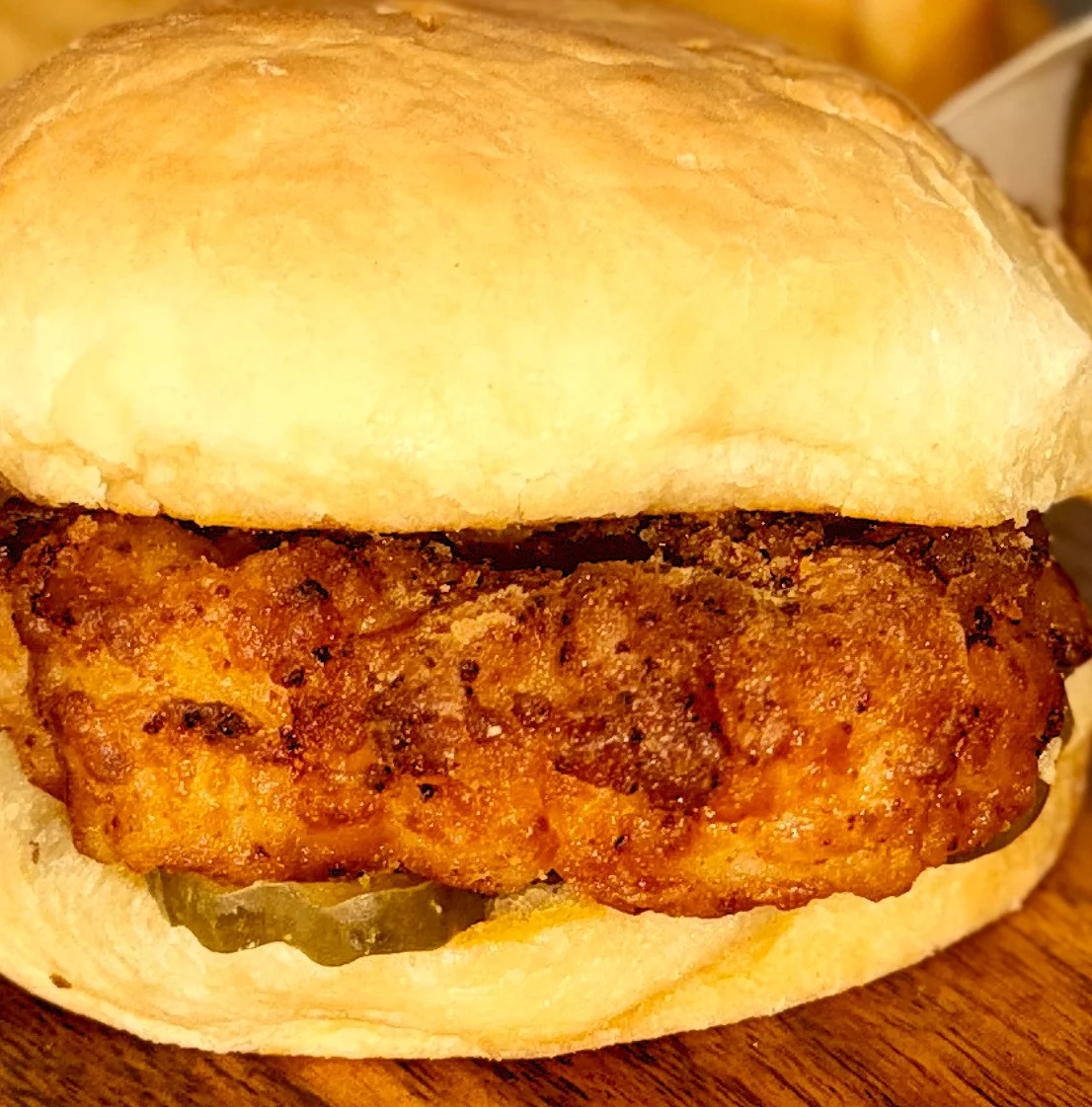 Fried chicken sandwich with pickles and fries on a wooden surface.