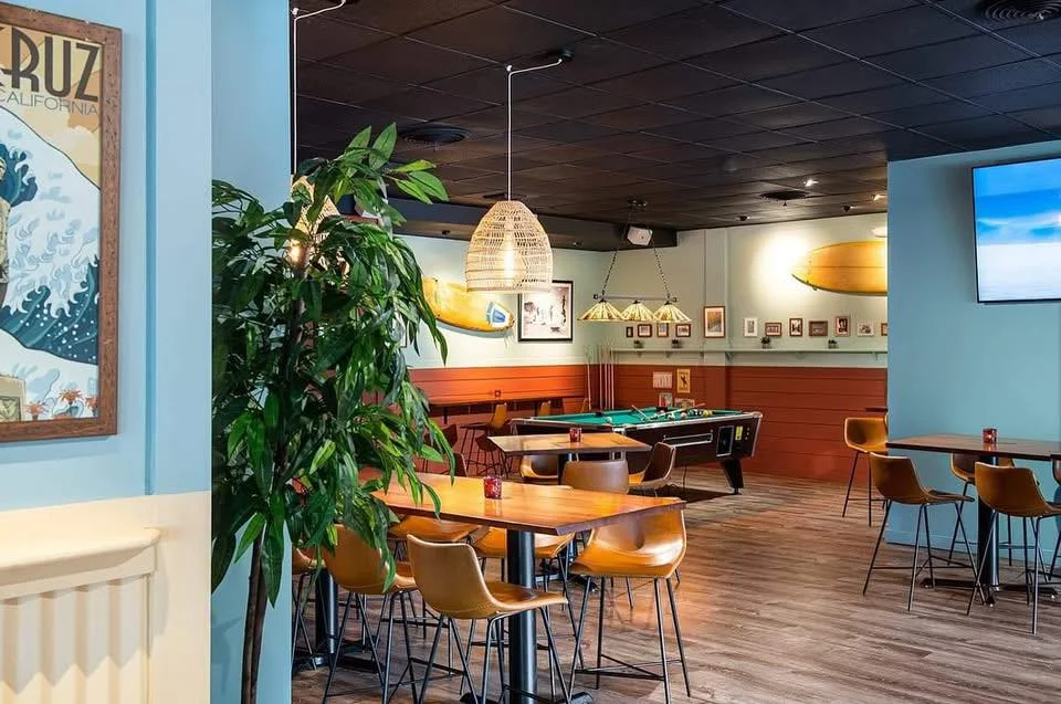 A cozy dining area featuring wooden tables, modern chairs, and a playful beach-themed decor. A pool table is visible in the background.