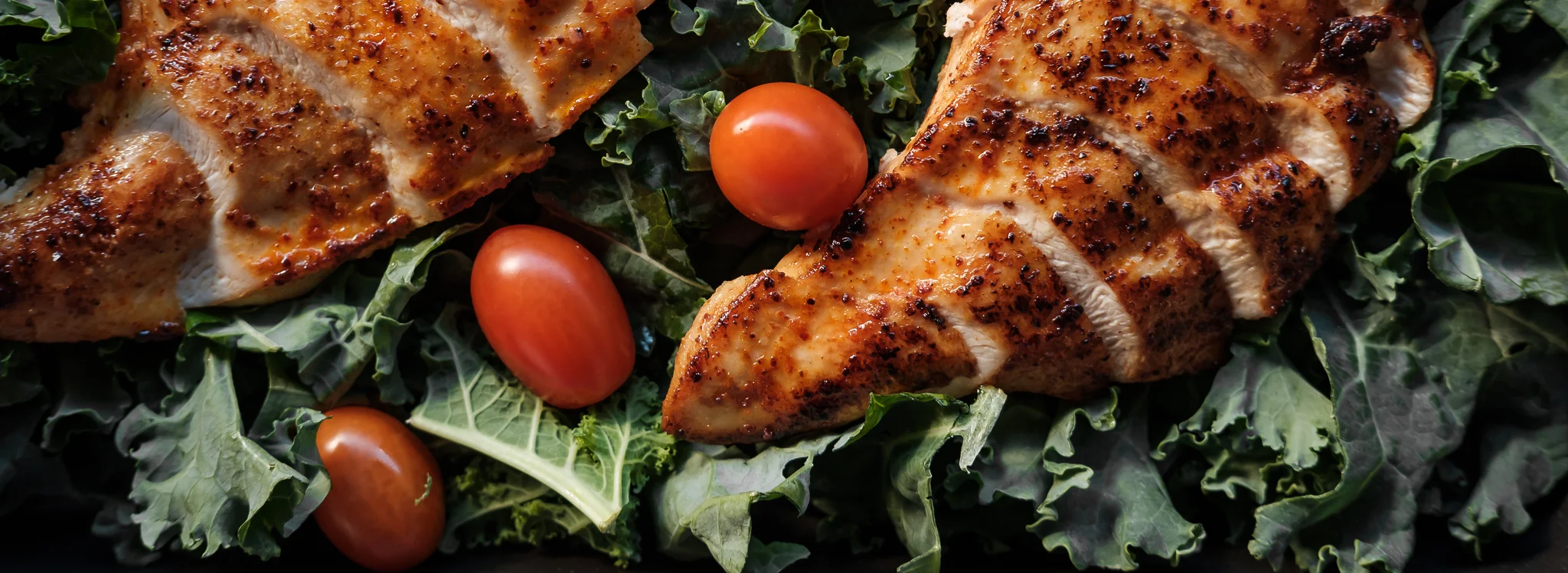 Grilled chicken breast on a bed of greens with cherry tomatoes